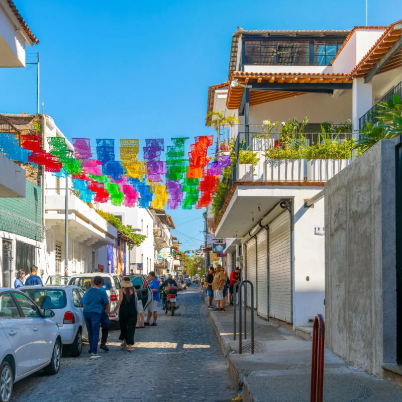 A street of homes and shops with colorful flags overhead in the Romantic Zone or Zona Romantica in Puerto Vallarta, Mexico.
