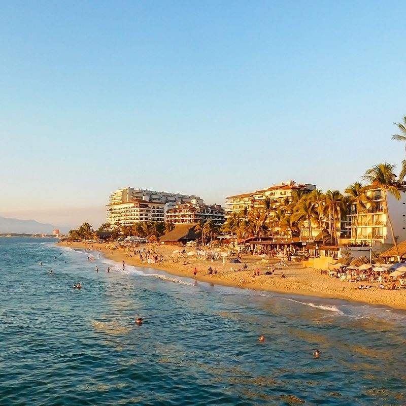 Puerto Vallarta sunset with calm waters, palm trees, tourists, and resorts