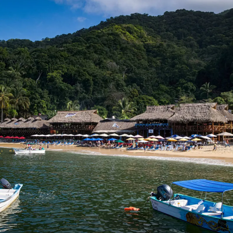 View of tied boats, Pichon Restaurant, and beach umbrellas at this small beachfront town just south of Puerto Vallarta and popular for swimming, and paragliding