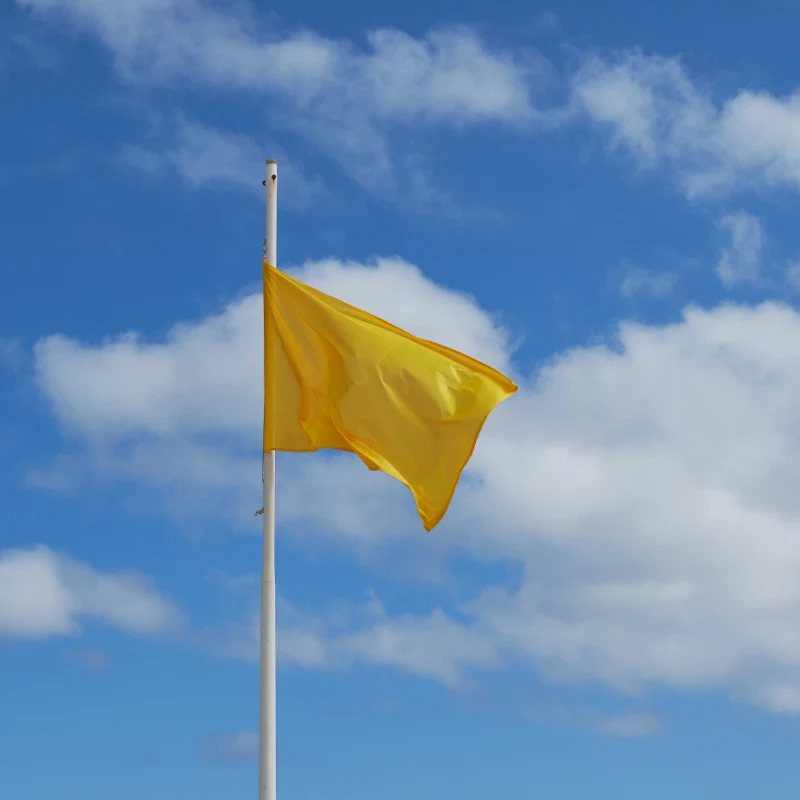 Yellow flag on a bluish sky with white clouds. Up view. Close up