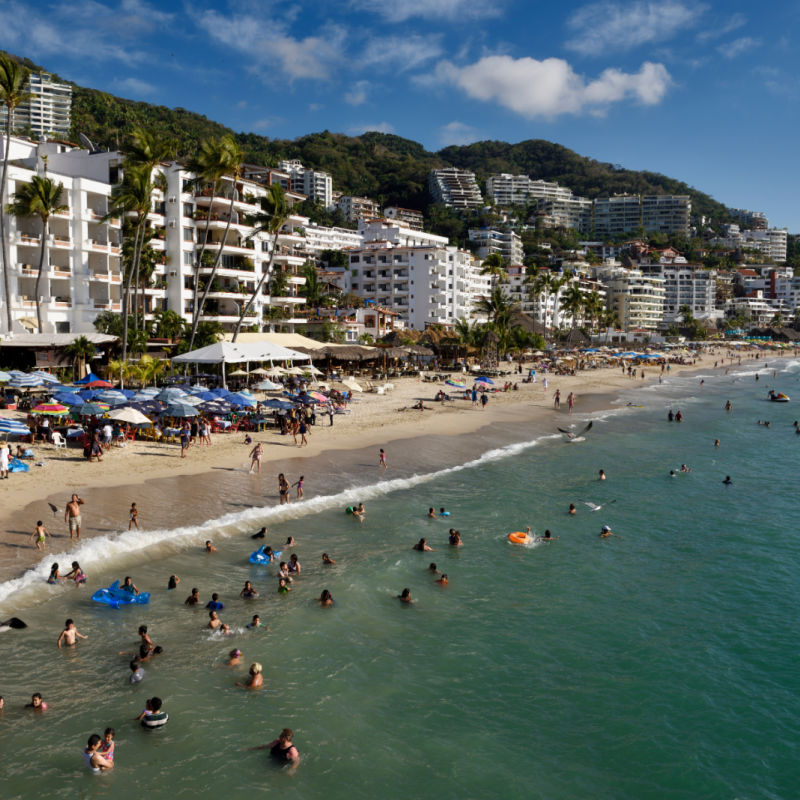People enjoying the beach on a sunny day in Puerto Vallarta. Buildings in the background