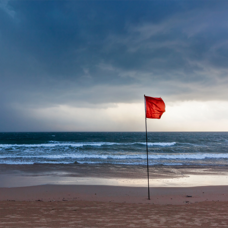 Red flag on beach with a cloudy sky