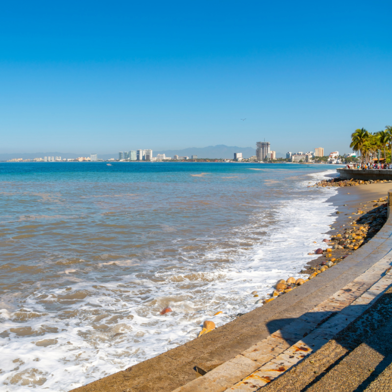 The sandy beach alongside the Malecon promenade boardwalk and Zona Romantica area of Puerto Vallarta, Mexico, with the sea and city skyline in view